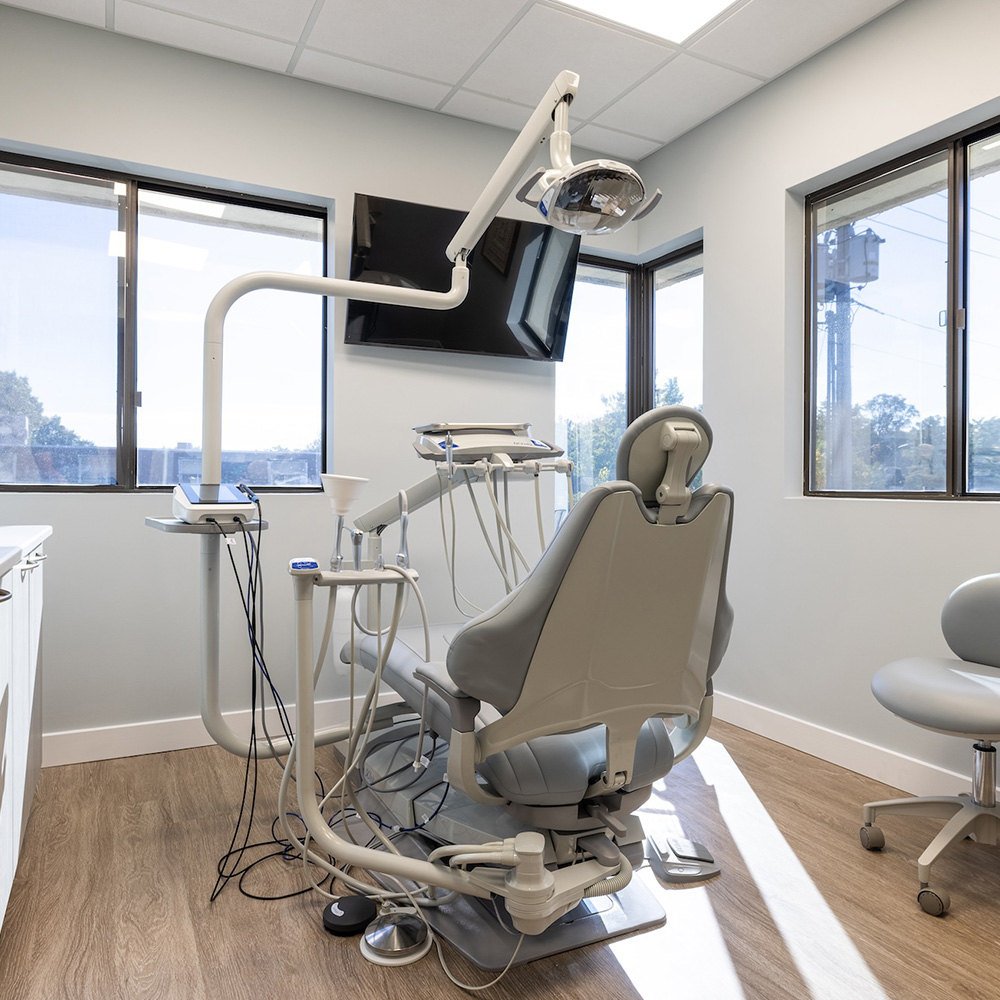 The image shows a dental office interior with modern equipment, including a dental chair and a computer monitor displaying what appears to be patient records or digital imaging.